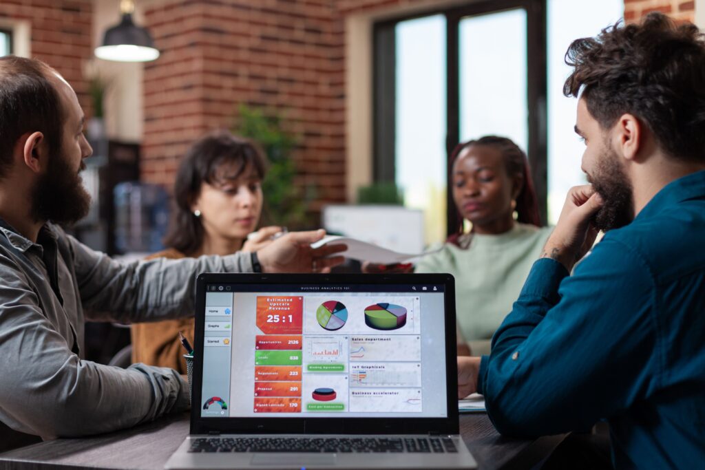 computador portatil com graficos de marketing na tela em pe na mesa no escritorio de inicializacao enquanto equipe diversa compartilhando papeis com a rotatividade da empresa empresarios multietnicas analisando a