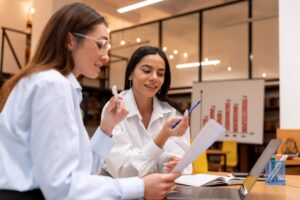 Mulheres trabalhando em sala de escritório com gráfico ao fundo.